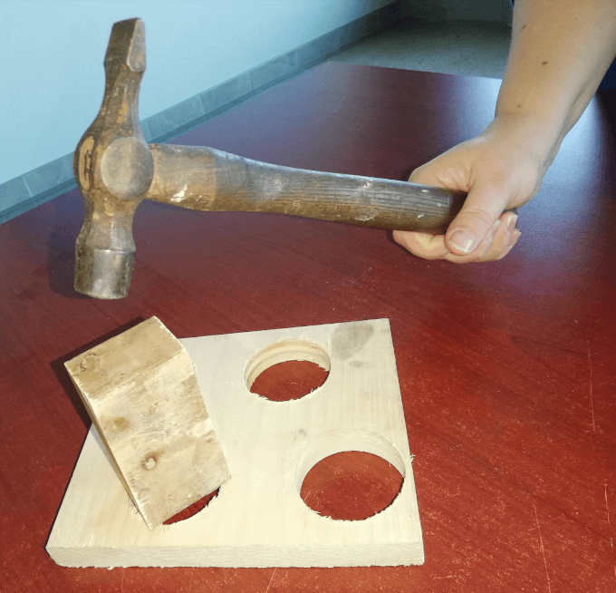 Person using a hammer on a block of wood